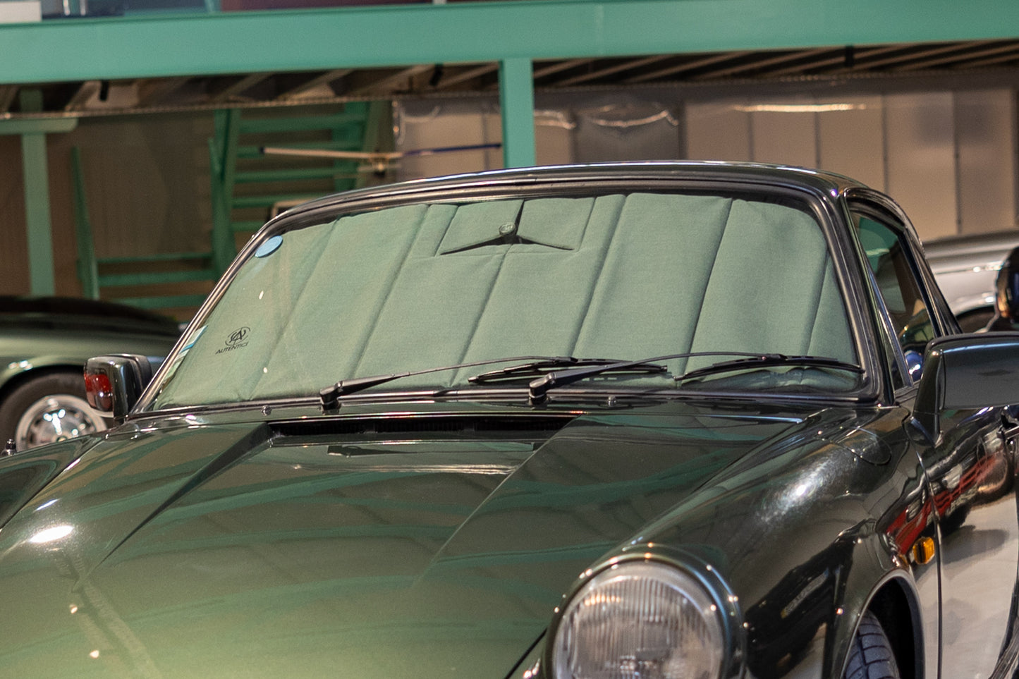 Green classic car fitted with a custom premium Autentici sunshade, highlighting tailored craftsmanship and superior sun protection. Autentici sun shade for car windshield. Protetor solar para para-brisas de automóvel clássico.