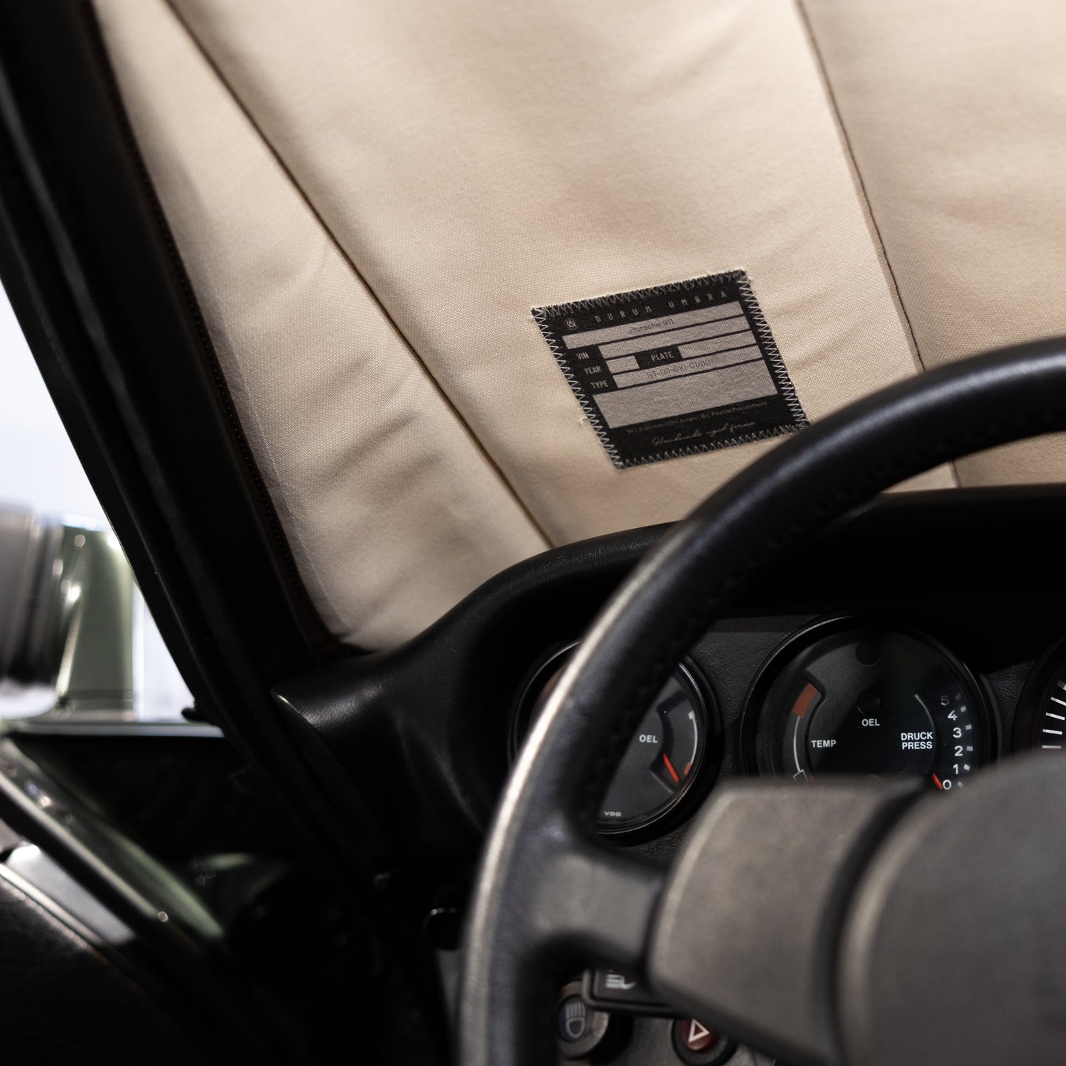Interior view of a classic car featuring a premium beige sunshade with a stitched label, highlighting custom craftsmanship and luxury car interior protection, Autentici sun shade for car windshield. Protetor solar para para-brisas de automóvel clássico.