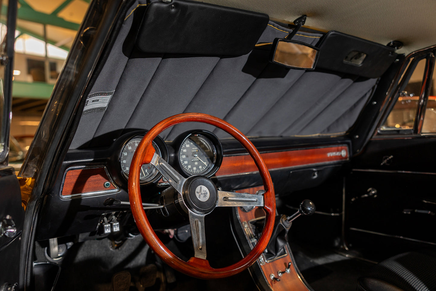 Interior of a classic car featuring a wooden steering wheel, vintage dashboard details, and a custom black sunshade installed, showcasing tailored interior protection and timeless elegance.Autentici sun shade for car windshield. Protetor solar para para-brisas de automóvel clássico.