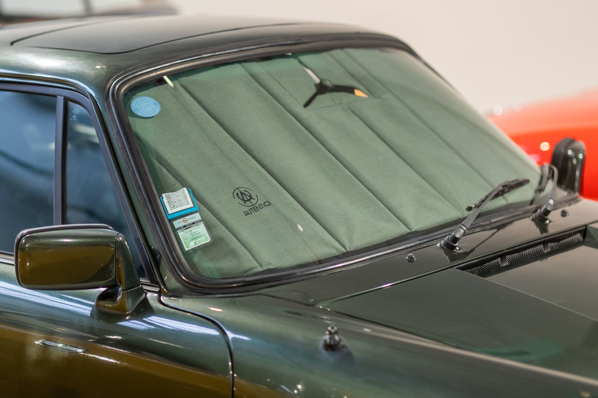 Close-up of a classic green car fitted with a premium green sunshade, highlighting custom design and windshield protection in a showroom setting.  Autentici sun shade for car windshield. Protetor solar para para-brisas de automóvel clássico.