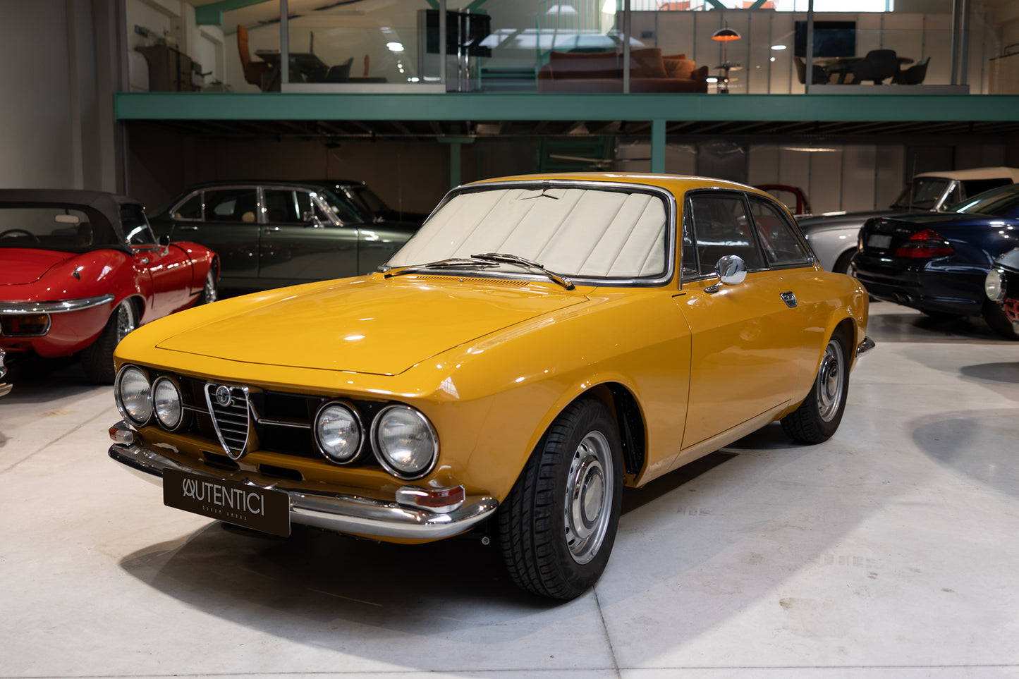 Classic yellow car fitted with a premium beige sunshade in an indoor showroom, showcasing luxury interior protection and timeless design. Autentici sun shade for car windshield. Protetor solar para para-brisas de automóvel clássico.