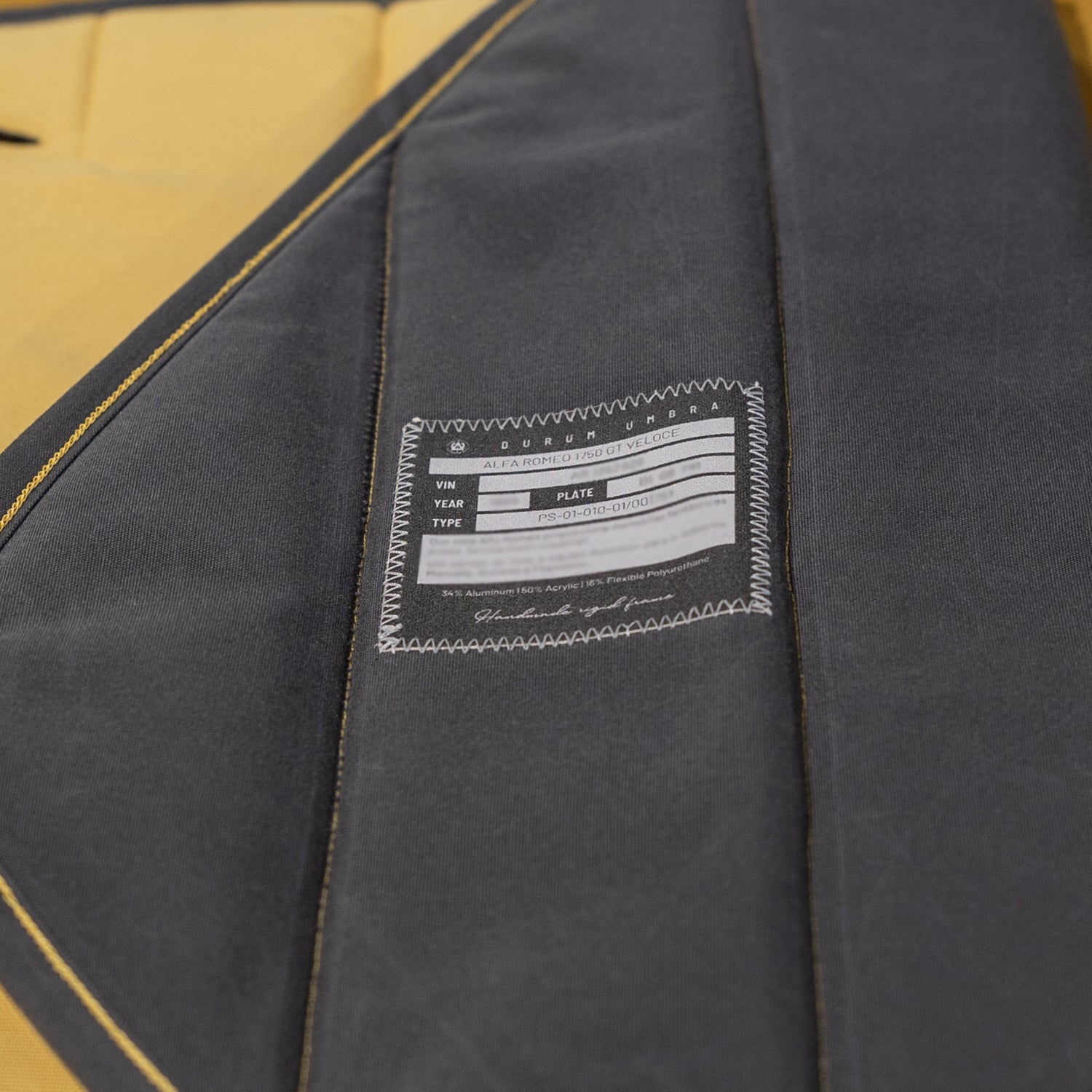 Close-up of a custom car sunshade in black and beige with a stitched label displaying the car model details, emphasizing luxury craftsmanship and tailored car interior protection. Autentici sun shade for car windshield. Protetor solar para para-brisas de automóvel clássico.