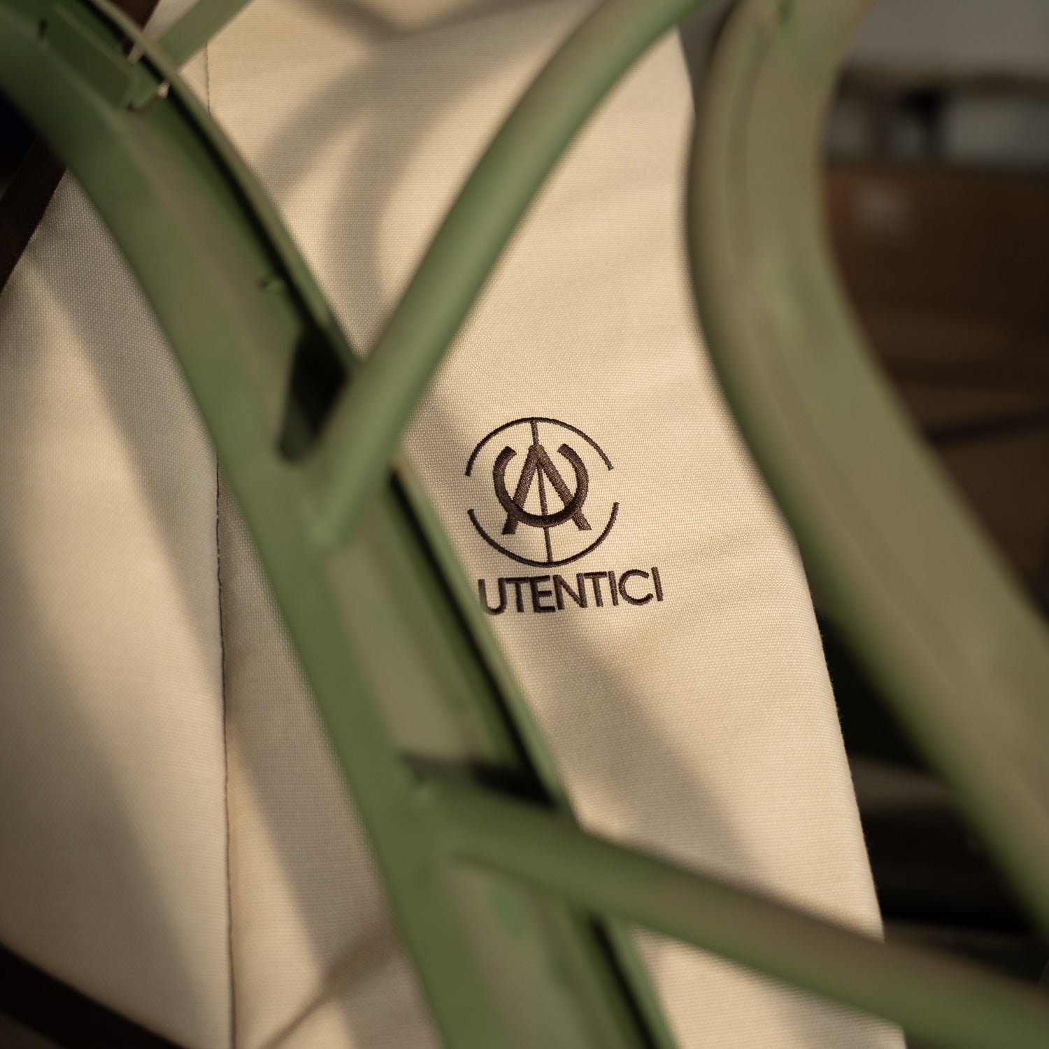 Close-up of a luxury handmade car accessory logo on a beige fabric, framed by a green aluminum structure, showcasing premium craftsmanship, Autentici