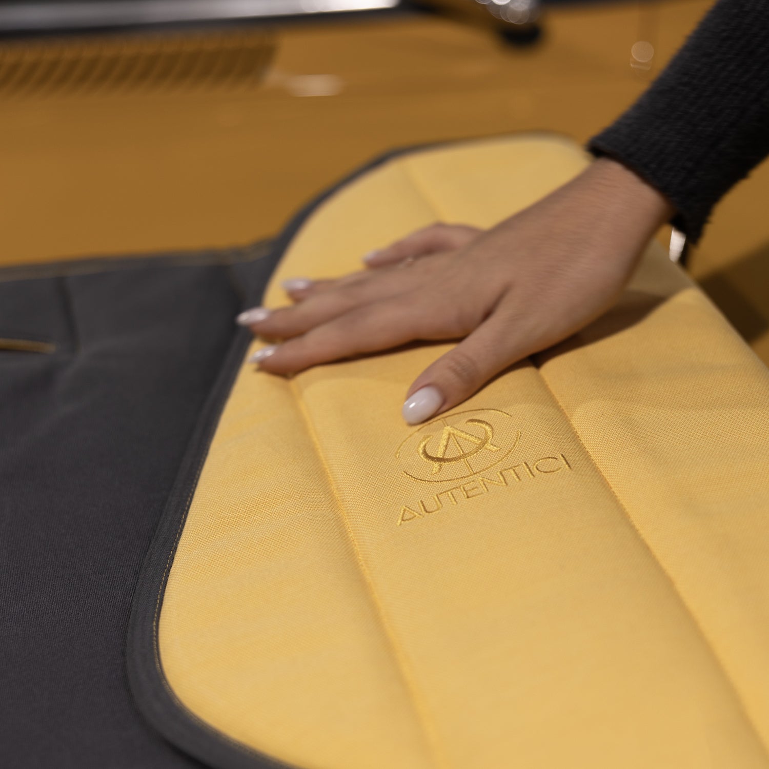 Hand touching a premium yellow and black custom car sunshade with an embroidered logo, highlighting luxury craftsmanship and tailored interior protection for classic cars. Autentici sun shade for car windshield. Protetor solar para para-brisas de automóvel clássico.